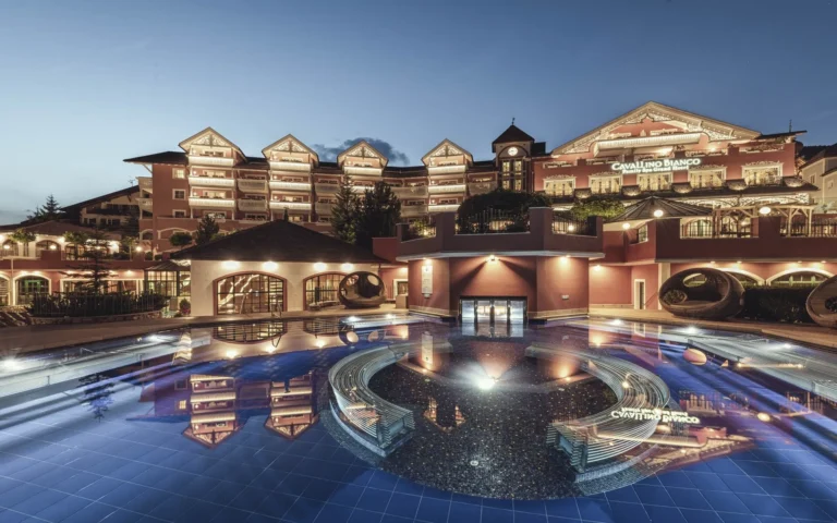 Cavallino Bianco Family Spa Grand Hotel illuminated at dusk, with outdoor pool