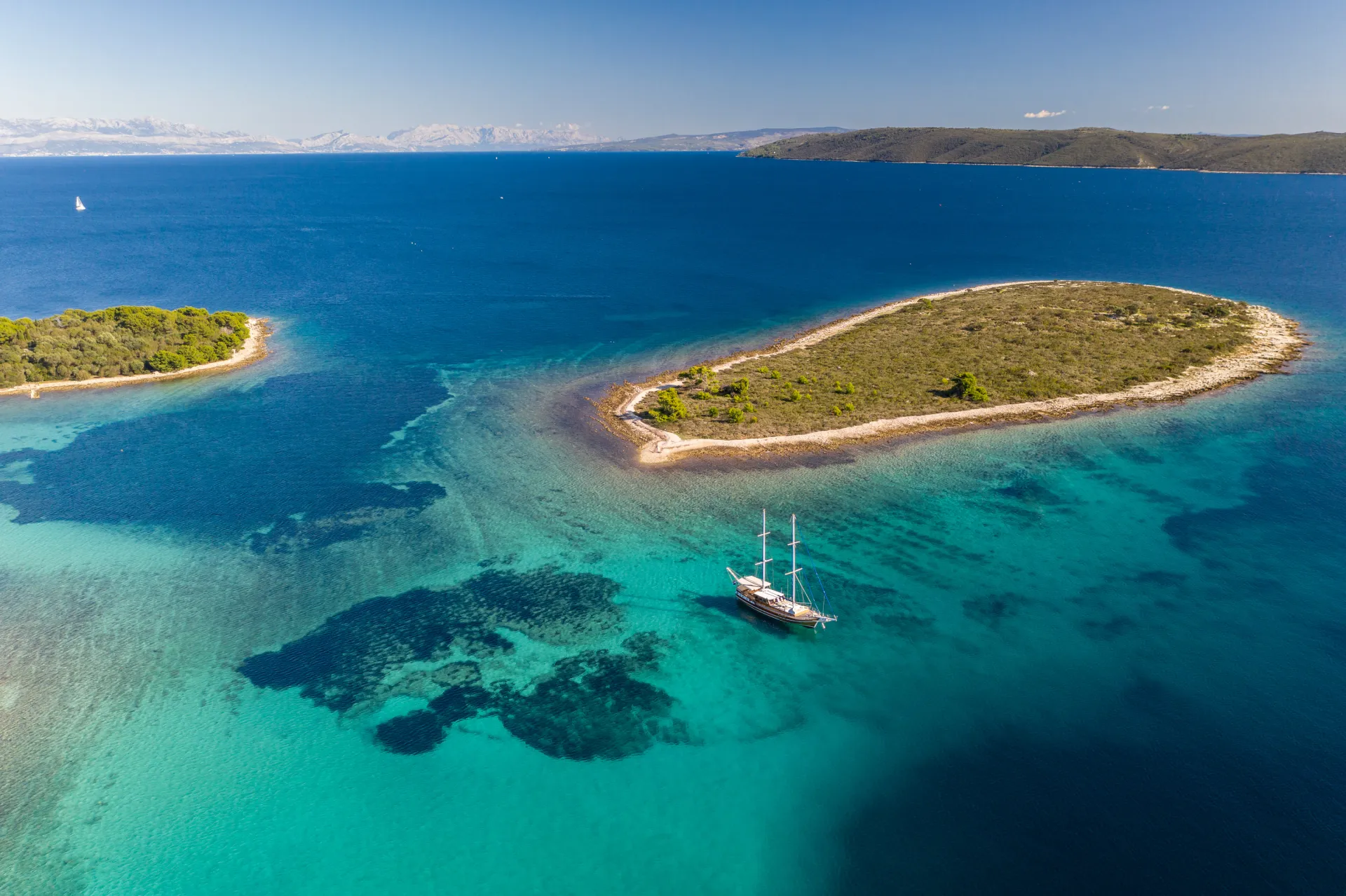 Aerial view of the gulet Andi Star anchored in clear turquoise water beside a small pine-covered Croatian island