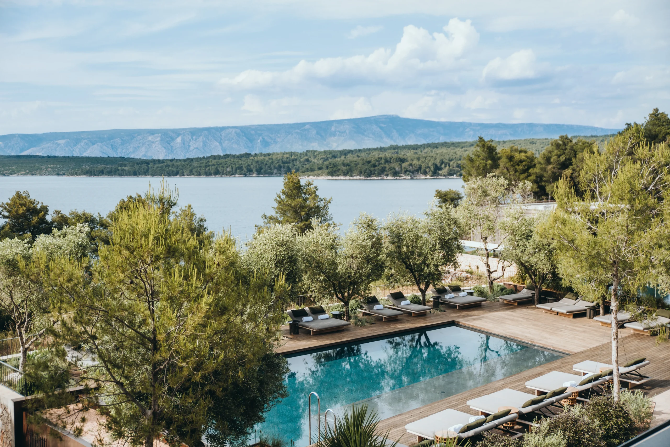 Outdoor pool on a wooden deck at Maslina Resort, surrounded by olive groves with the Stari Grad bay and hills beyond