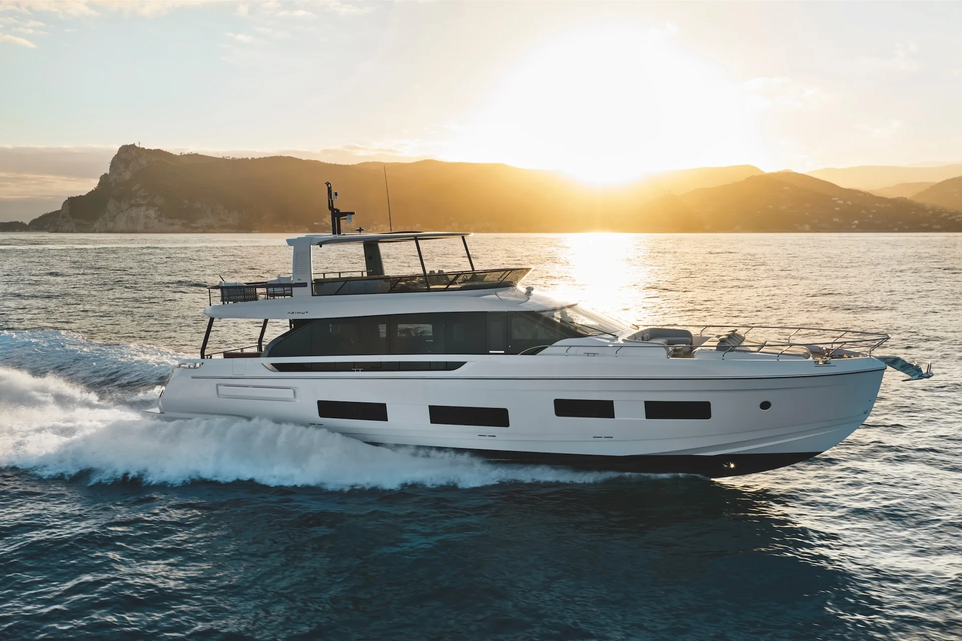 An Azimut 82 Fly motor yacht running at speed past a headland in low evening sun