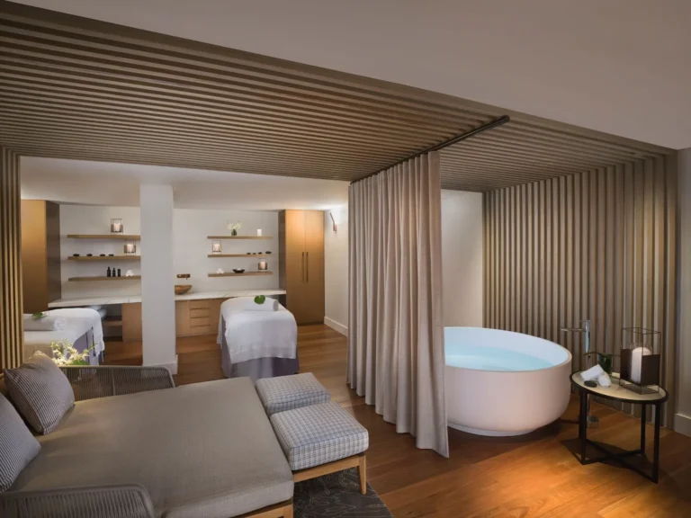 Spa treatment room with two massage beds and a freestanding bath behind a curtain