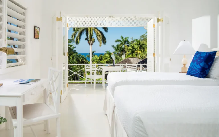 Twin beds in a white room with balcony doors and a view over treetops and sea