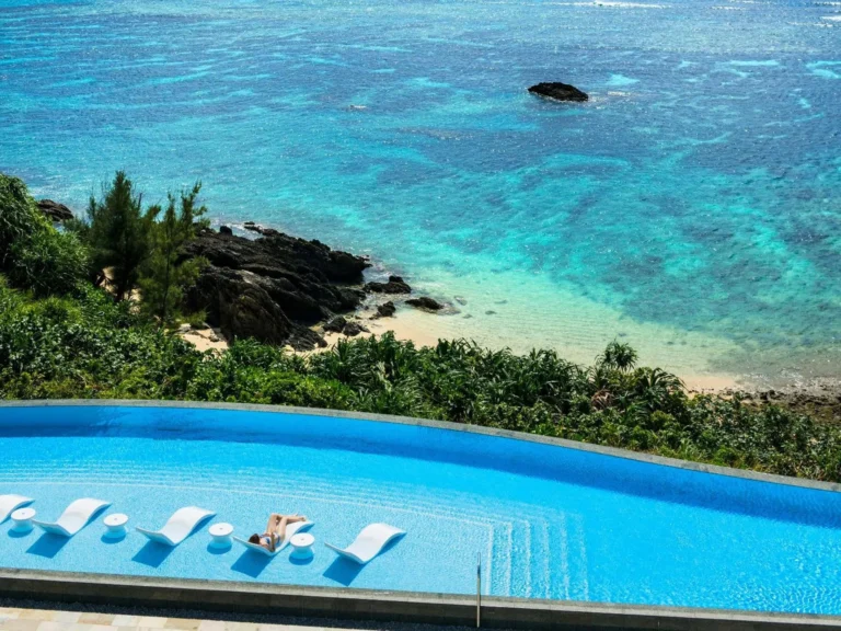 Infinity pool with in-water loungers above a cove of turquoise water