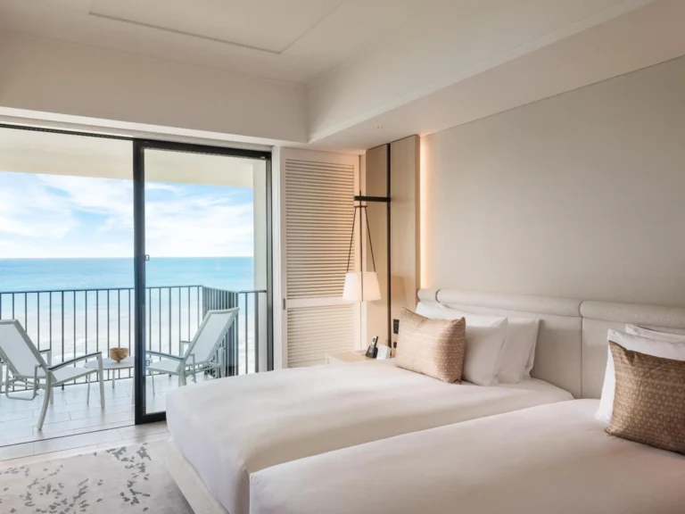 Twin beds beside a balcony with two loungers and a sea view
