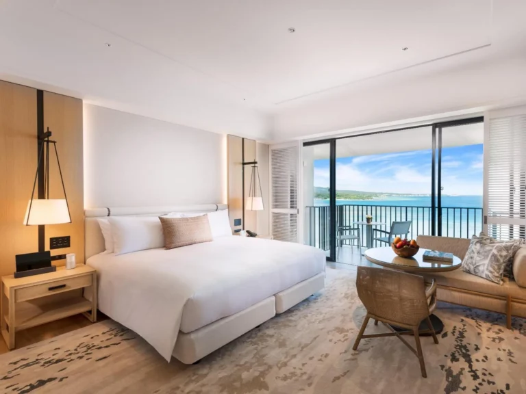 King bed with a sofa and a round table in front of a sea-view balcony