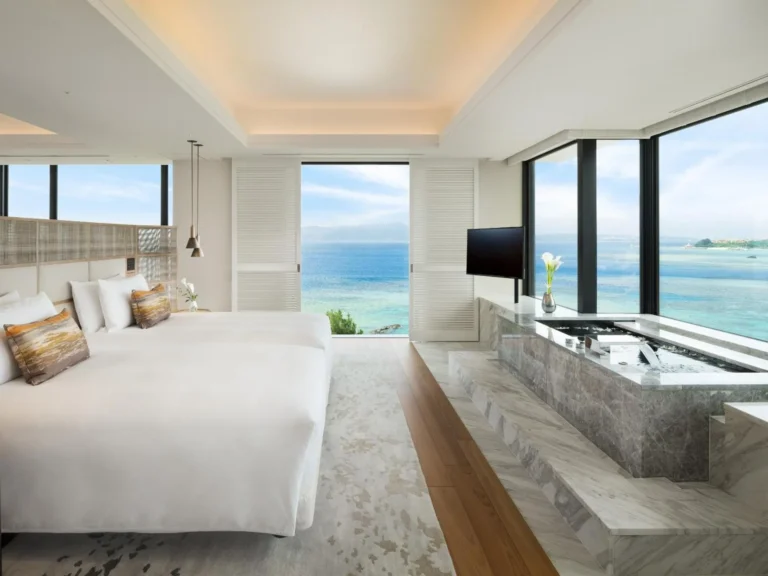 Suite bedroom with twin beds, a sunken tub beside the window and a view of the sea