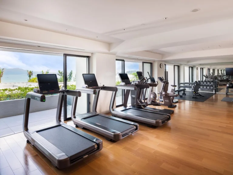 Treadmills and weights in a gym with wooden floor and sea-view windows