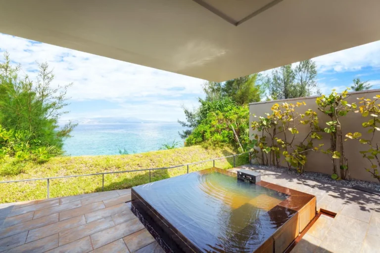 Dark wooden hot spring bath on a villa terrace above grass and the sea