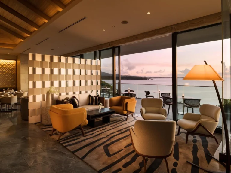 Club lounge seating in orange armchairs beside floor-to-ceiling glass at dusk