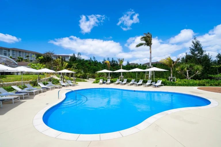 Free-form blue pool with parasols and loungers on lawn beside the hotel building