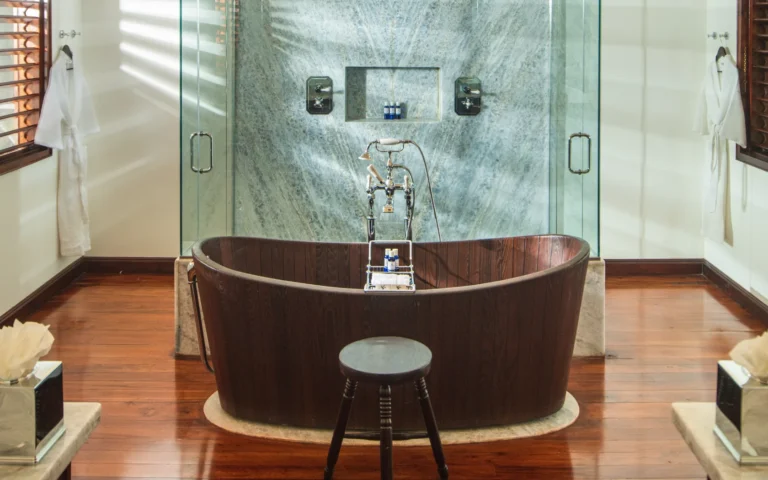 Freestanding dark wooden bathtub and glass shower on a polished wooden floor