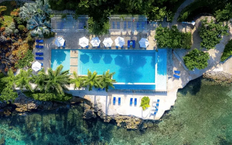 Aerial view of the oceanside swimming pool with white umbrellas and loungers at the rock edge