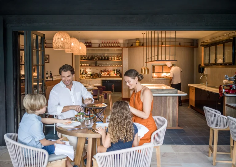 A mother, father and two children at a round table in front of an open pizza kitchen