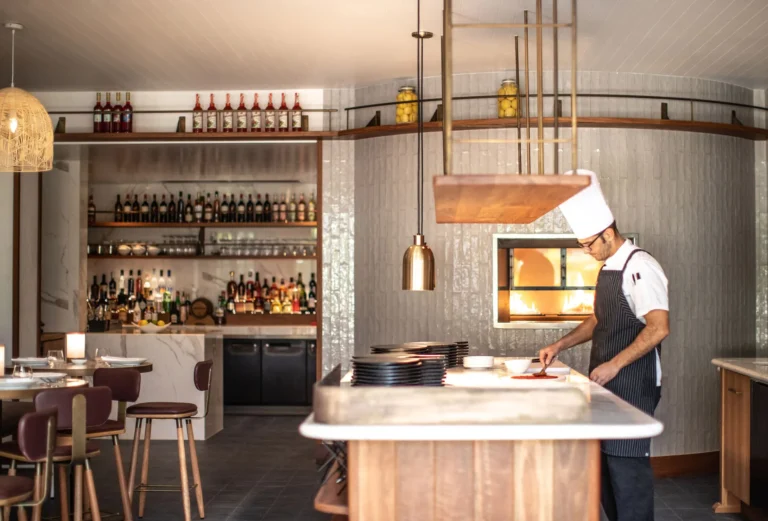 A chef shaping a pizza at the counter beside a wood-fired oven