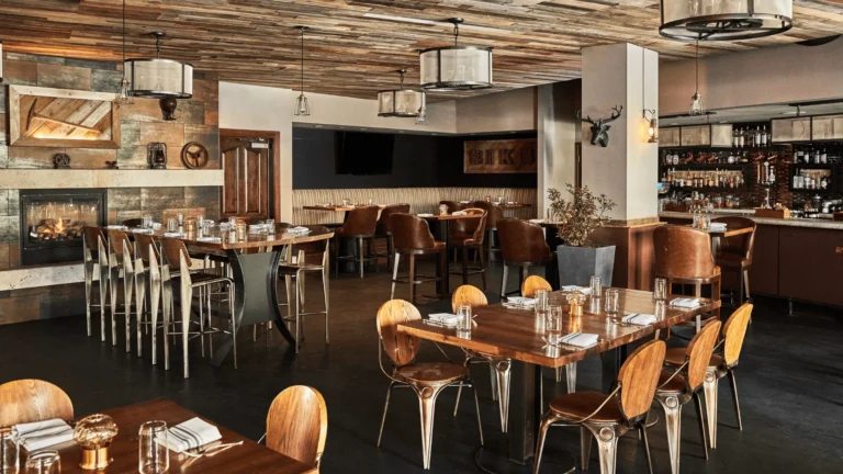 Black Iron Kitchen + Bar dining room with wooden tables, tall chairs and a stone fireplace
