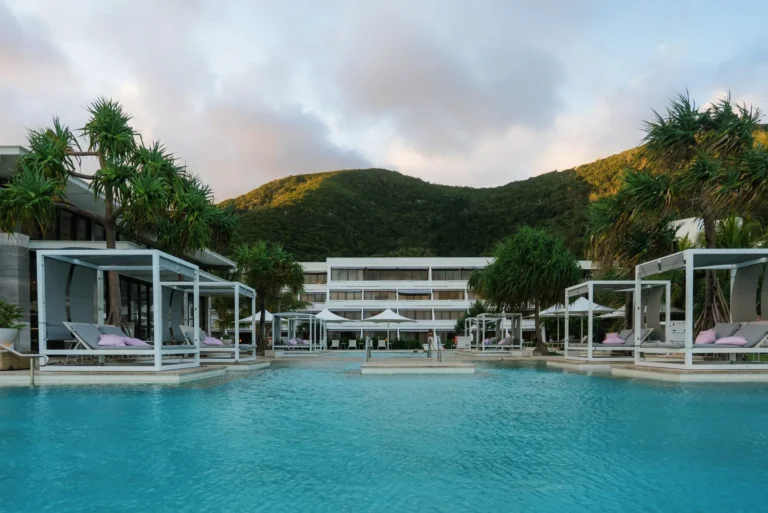 Pool with white daybed cabanas and a resort wing beneath green hills