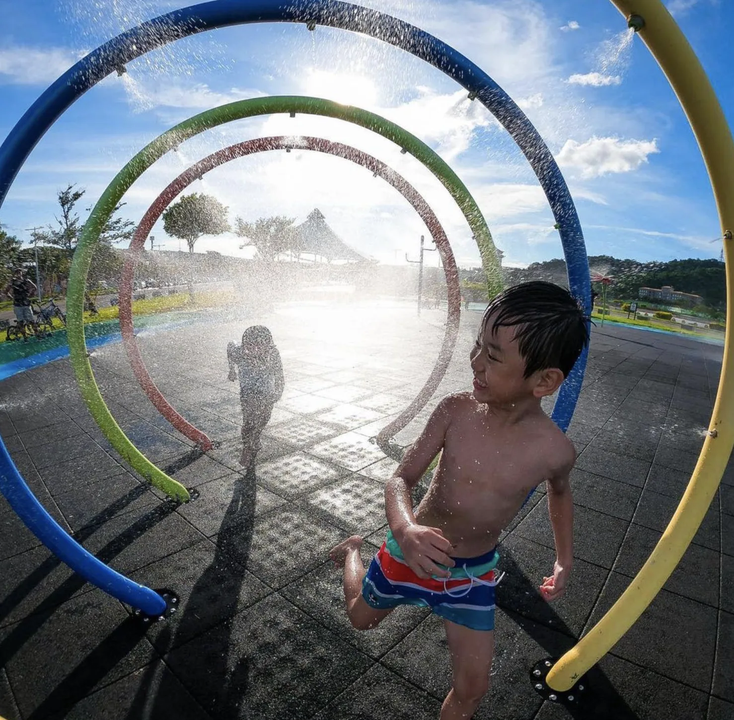 A boy runs through colourful sprinkler arches at a water playground.