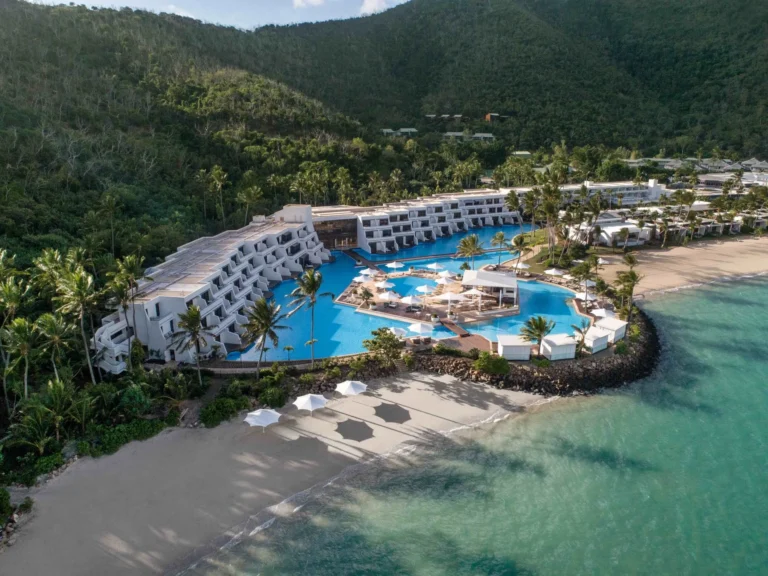 Aerial view of the curved resort wings, central pool and beach on Hayman Island