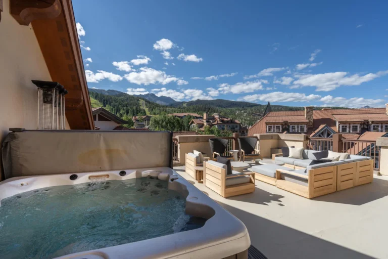 Rooftop terrace with a built-in hot tub and wooden lounge furniture above Mountain Village rooftops