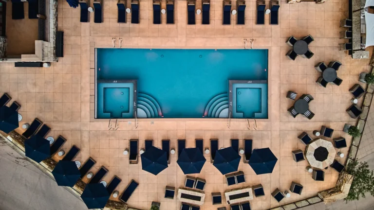 Top-down view of the rectangular pool and hot tub with surrounding loungers, umbrellas and fire-pit tables