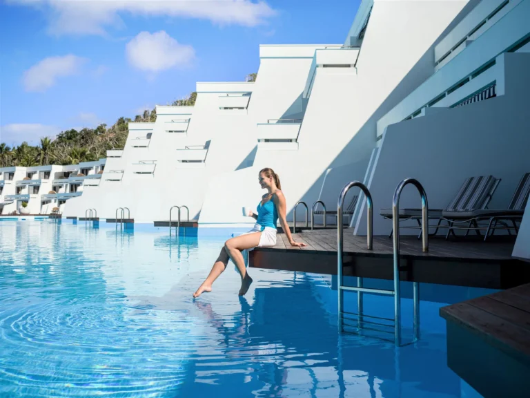 A woman sitting on the pool edge beside stepped white wings of swim-out suites