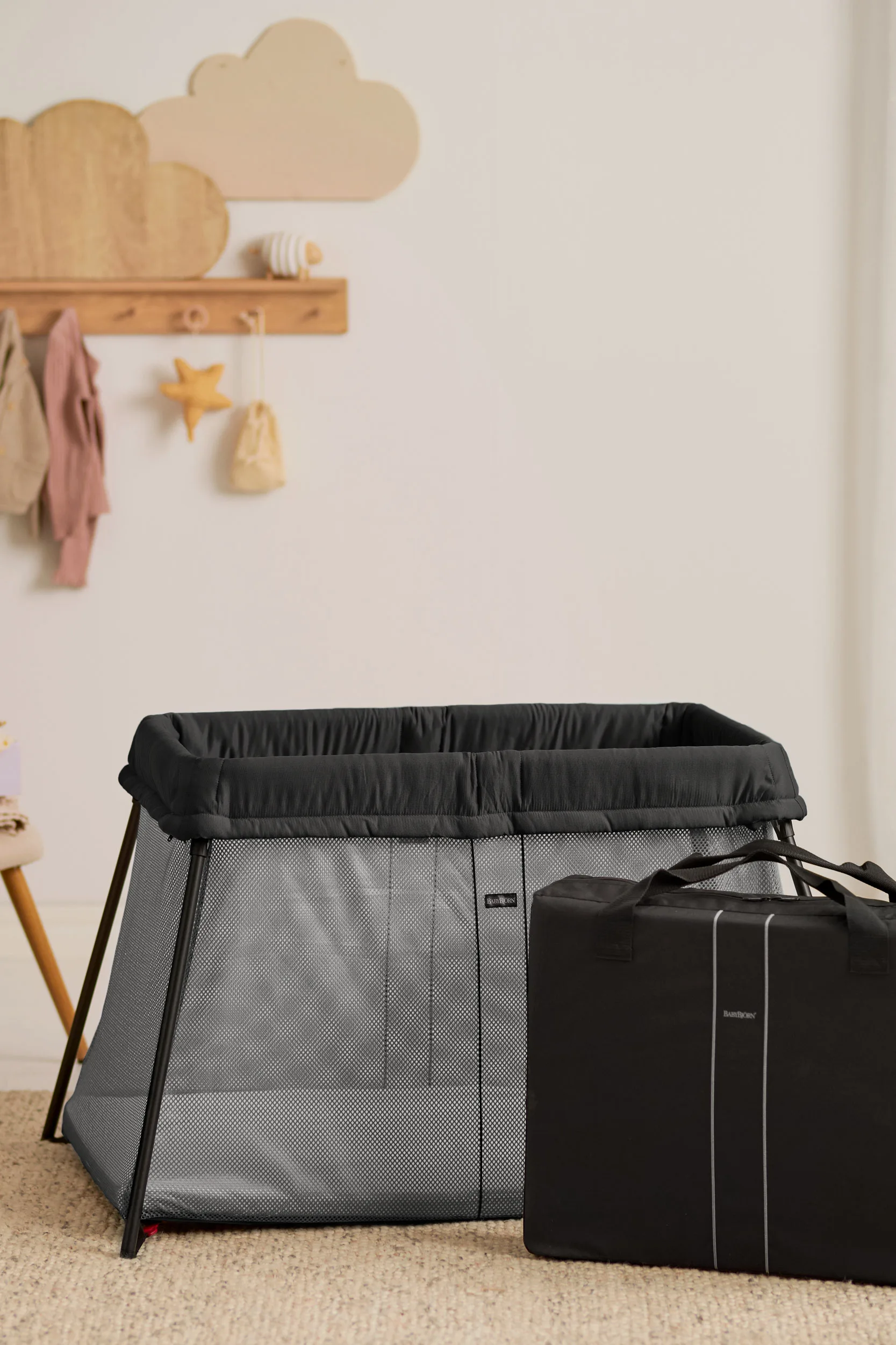 Black mesh BabyBjörn Travel Cot Light assembled beside a bed, with its supplied mattress visible
