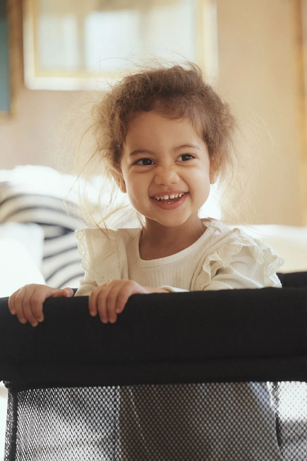 BabyBjörn Travel Cot Light set up with a clear approach beside a bed and luggage stored away