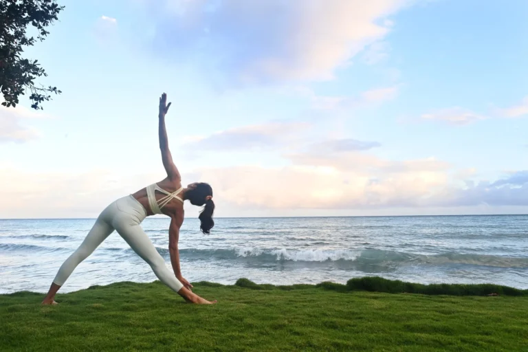 Woman in a triangle yoga pose on a grassy edge above the sea
