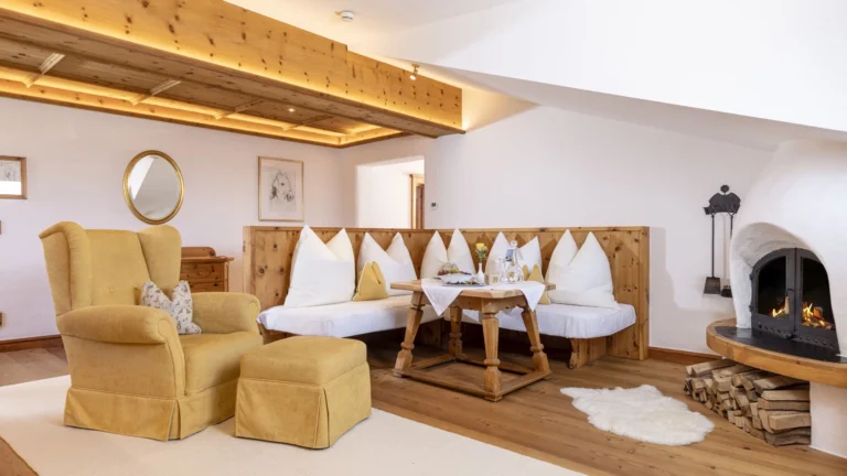 Suite sitting area with a corner bench of white cushions, a yellow armchair and a tiled stove with a lit fire