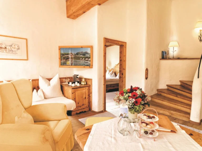 Family suite living room with a yellow armchair, set table, timber stairs and an open door into the bedroom