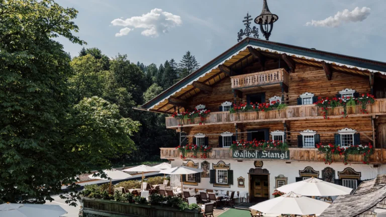 Multi-storey Gasthof Stangl with red flower boxes on timber balconies and parasols on the terrace in front