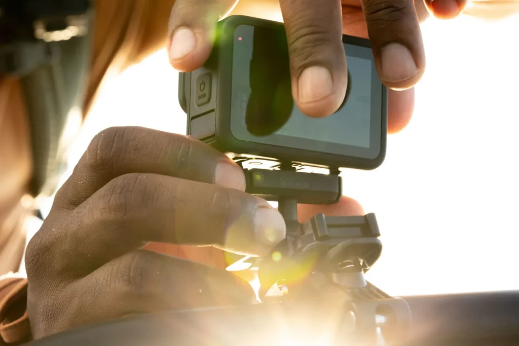 Hands fit a GoPro camera onto a mount, backlit by low sun.