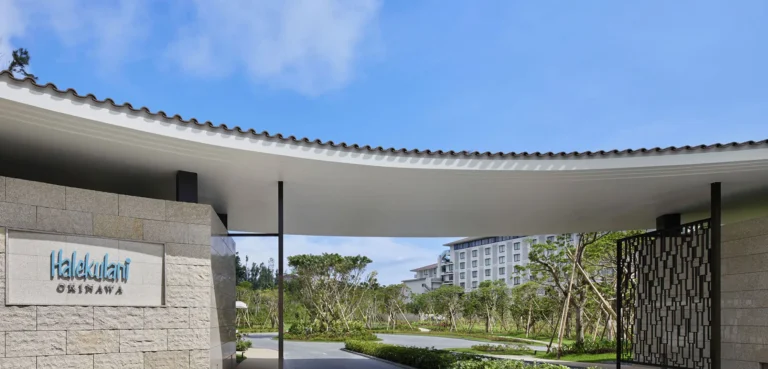 Curved roof porte-cochere with the Halekulani Okinawa sign on a limestone wall and the hotel beyond