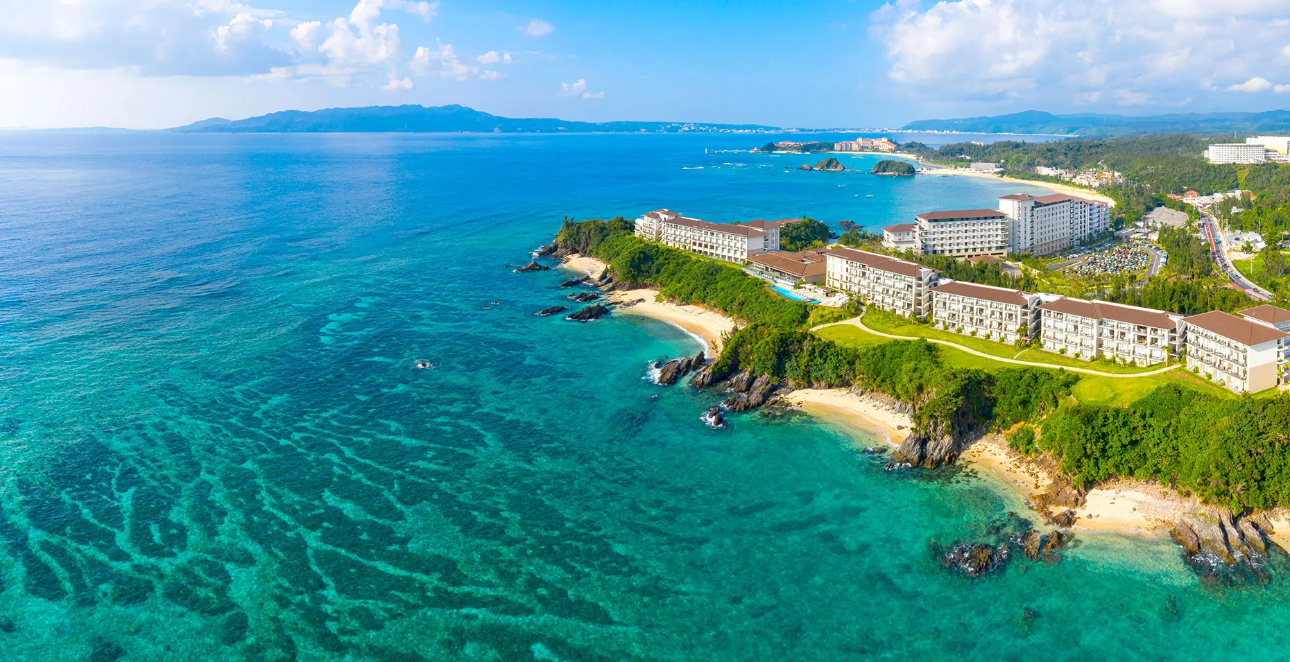 Aerial view of the Halekulani Okinawa buildings along a green headland above turquoise reef water