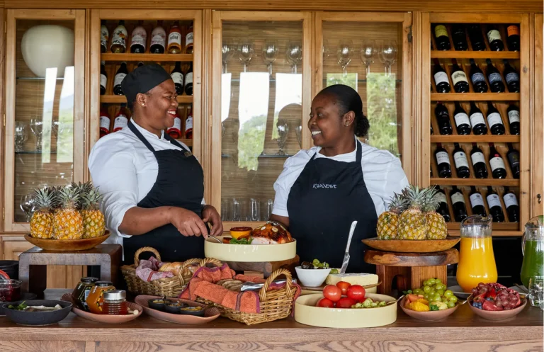 Two members of the kitchen team behind a breakfast spread of fruit and juices at Kwandwe Ecca Lodge
