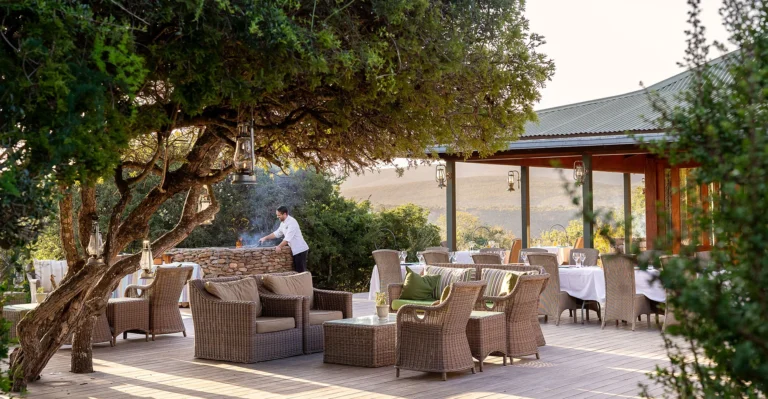 Outdoor lounge and dining terrace at the main area of Kwandwe Ecca Lodge, set among trees