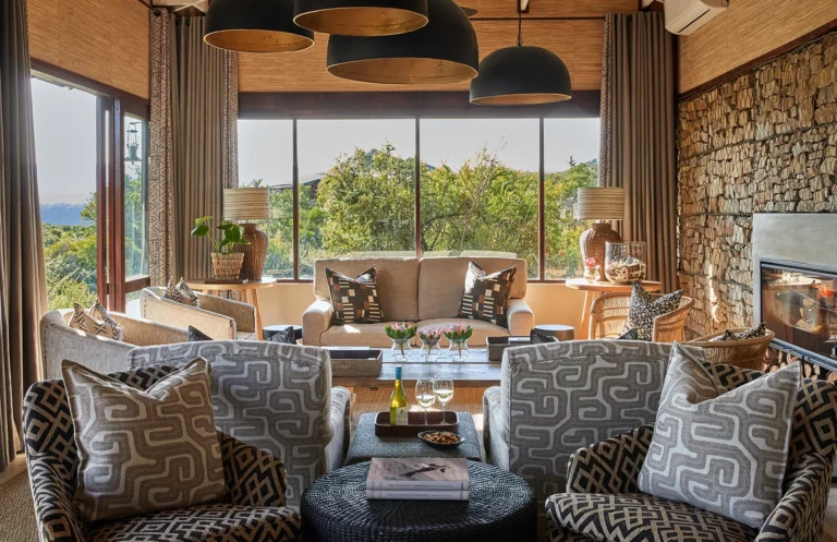 The main lounge at Kwandwe Ecca Lodge with a stone fireplace and patterned armchairs