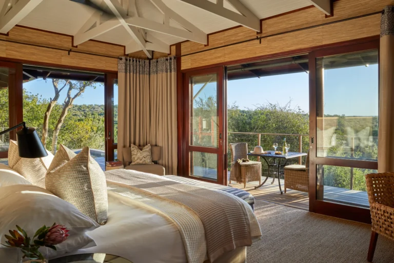 A suite bedroom at Kwandwe Ecca Lodge with floor-to-ceiling glass opening onto the bush