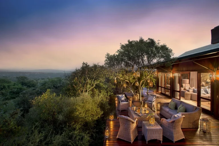 The main deck at Kwandwe Ecca Lodge at dusk, with wicker seating and lanterns