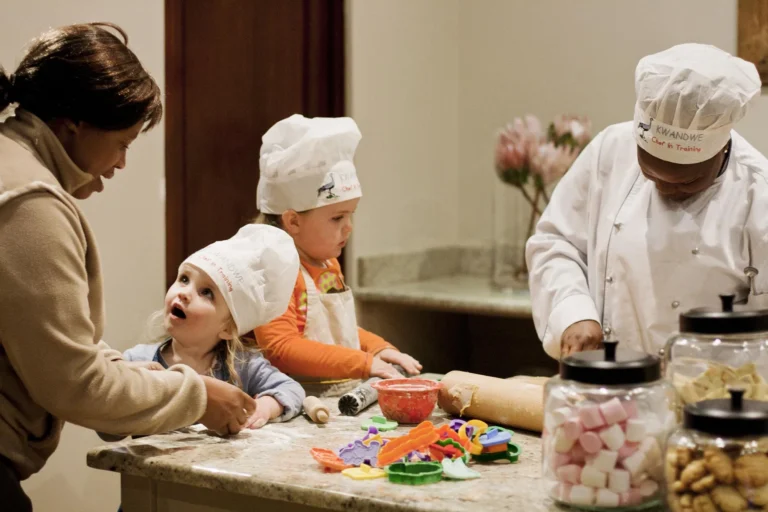 Two children in chef's hats baking with a chef and a member of staff at Kwandwe Ecca Lodge