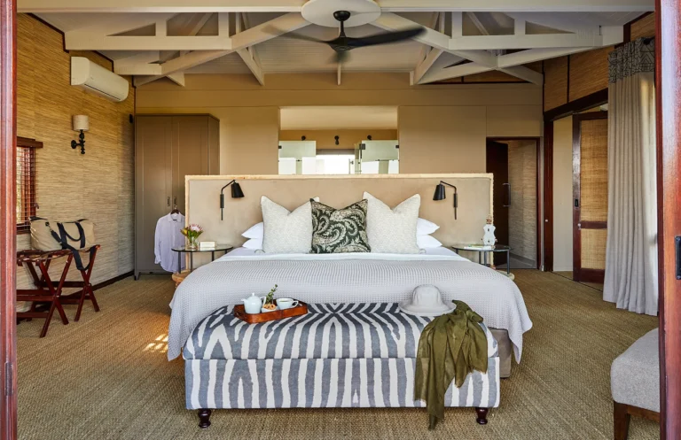 A suite bedroom at Kwandwe Ecca Lodge with a striped bench at the foot of the bed