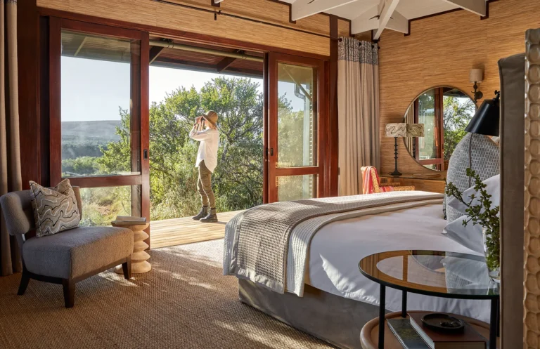 A suite bedroom at Kwandwe Ecca Lodge opening onto the deck, with a guest looking out over the valley