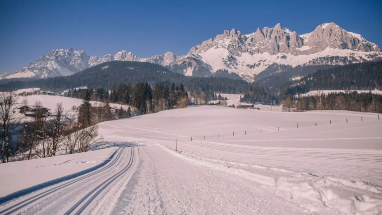 Groomed cross-country ski tracks running across a snowy meadow toward the Wilder Kaiser massif