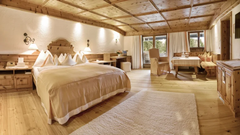 Large bedroom with a double bed, timber-panelled ceiling, writing desk and a seating area by terrace doors