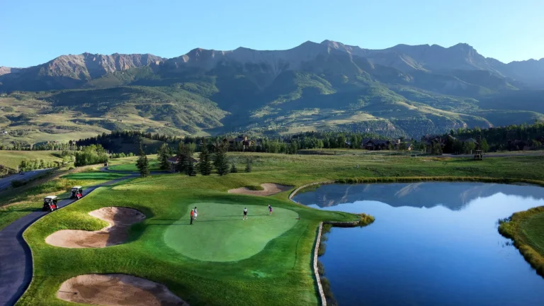 Telluride golf course with sand bunkers, a pond and a green fairway beneath a mountain ridge