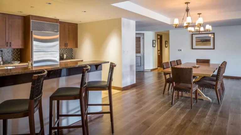 Full residence kitchen with wooden cabinets, steel fridge, range and island seating, dining table beyond