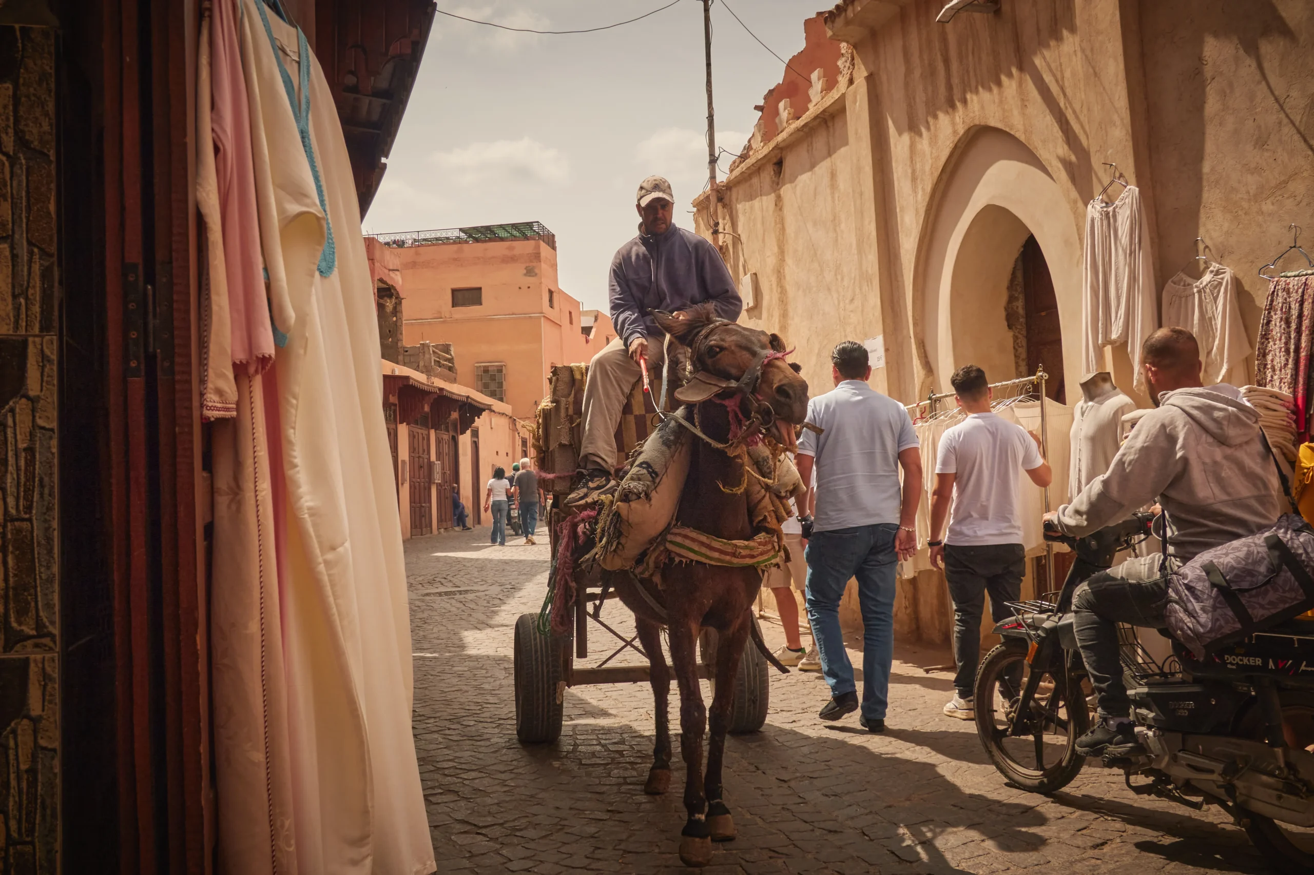 Narrow laneway in the Marrakech medina with colourful stalls and pedestrians.