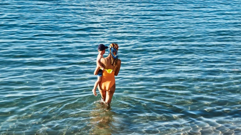 Mother carrying a toddler into calm sea water