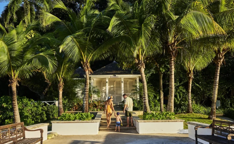 Two parents and a young child walking up steps toward a small white cottage under tall palms