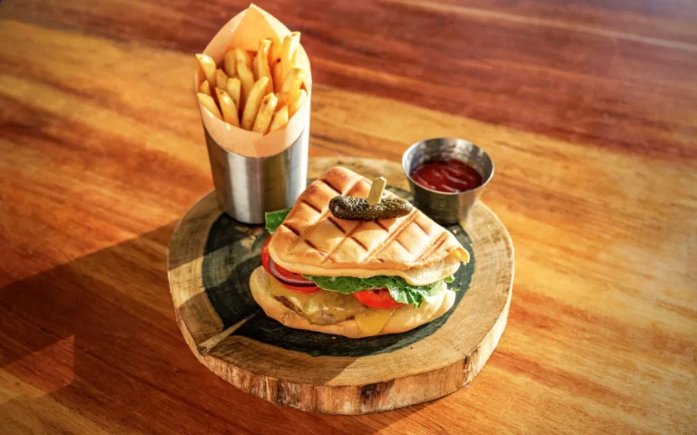 Toasted sandwich with fries in a paper cone and ketchup on a wooden board